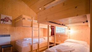 Una cabaña de madera con literas, una mesita y un ventanal con cortinas.