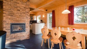 Acogedor interior de cabaña con chimenea de piedra, mesa de comedor de madera y sillas.