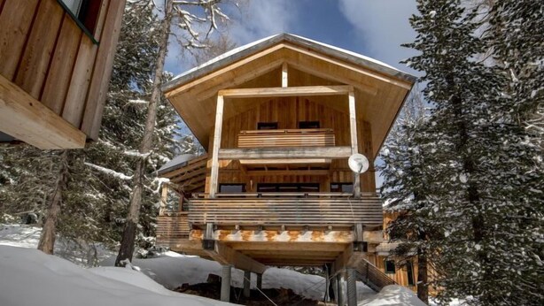 Una cabaña de madera con balcón, rodeada de árboles cubiertos de nieve.