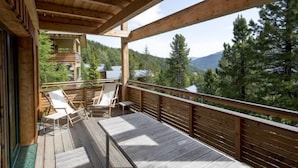 Eine Holzdiele mit zwei Liegestühlen und einem Tisch, mit Blick auf ein bewaldetes Tal.