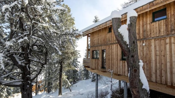 Eine Holzhütte mit einer Terrasse, umgeben von schneebedeckten Bäumen.