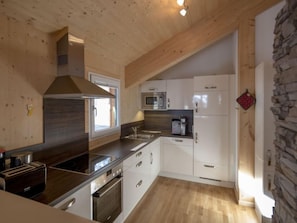 Cozinha moderna com vigas de madeira no teto, armários brancos, forno embutido e parede decorada com pedra.