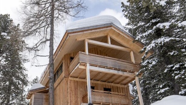 Eine Holzhütte mit Balkon, umgeben von schneebedeckten Bäumen.