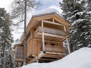 A wooden cabin with a balcony, surrounded by snow-covered trees.