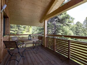A wooden deck with a round table and chairs, surrounded by a wooden railing, overlooking a forested area.