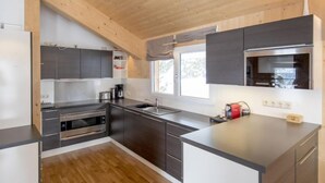 Eine moderne Küche mit dunklen Schränken, einem Edelstahlbackofen und einem großen Fenster, das für natürliches Licht sorgt.