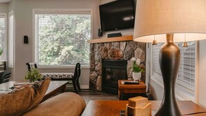 A cozy living room with a stone fireplace, a flat-screen TV mounted above it, a comfortable sofa, a coffee table, and a lamp.