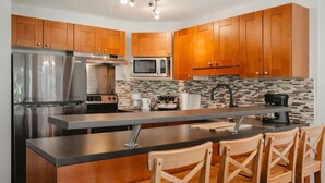 A modern kitchen with wooden cabinets, stainless steel appliances, a large island with bar stools, and a tiled backsplash.