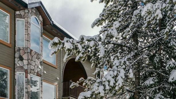 A multi-story building with stone and wood exterior, a covered entrance, and snow-covered surroundings.