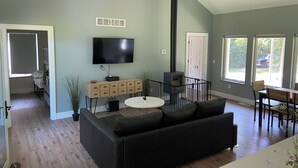 Una sala moderna con un sofá negro, un televisor montado en la pared, un mueble de madera y una chimenea.