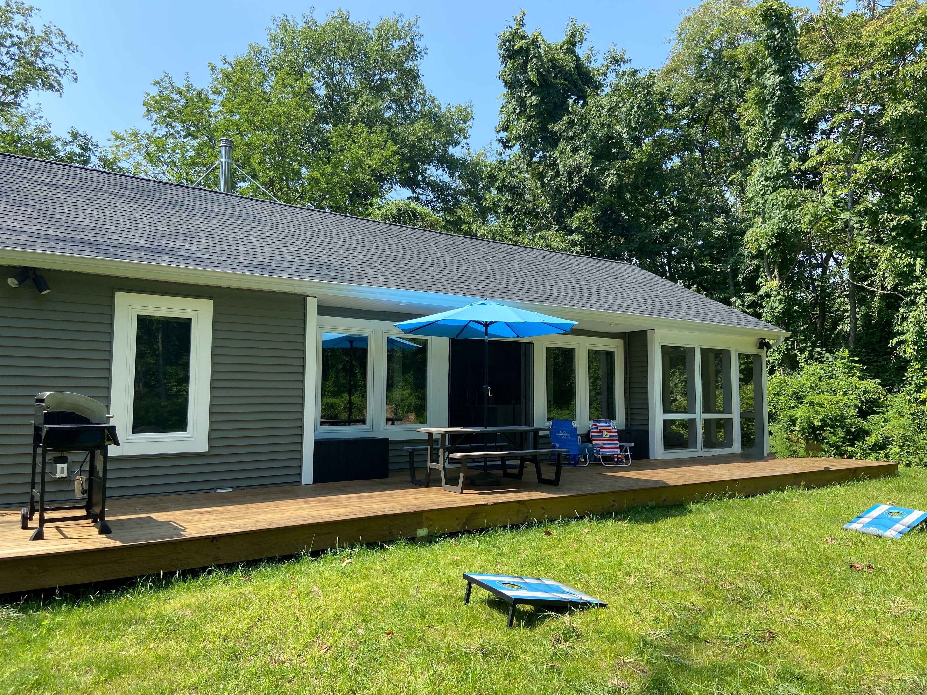 A house with a covered porch, a grill, and a table with chairs.