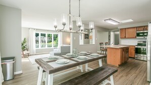 Una cocina moderna con armarios de madera, un refrigerador de acero inoxidable y un comedor con mesa y bancos.