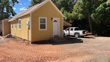 A small yellow building with a white door and windows, a gravel driveway, and a white pickup truck parked nearby.