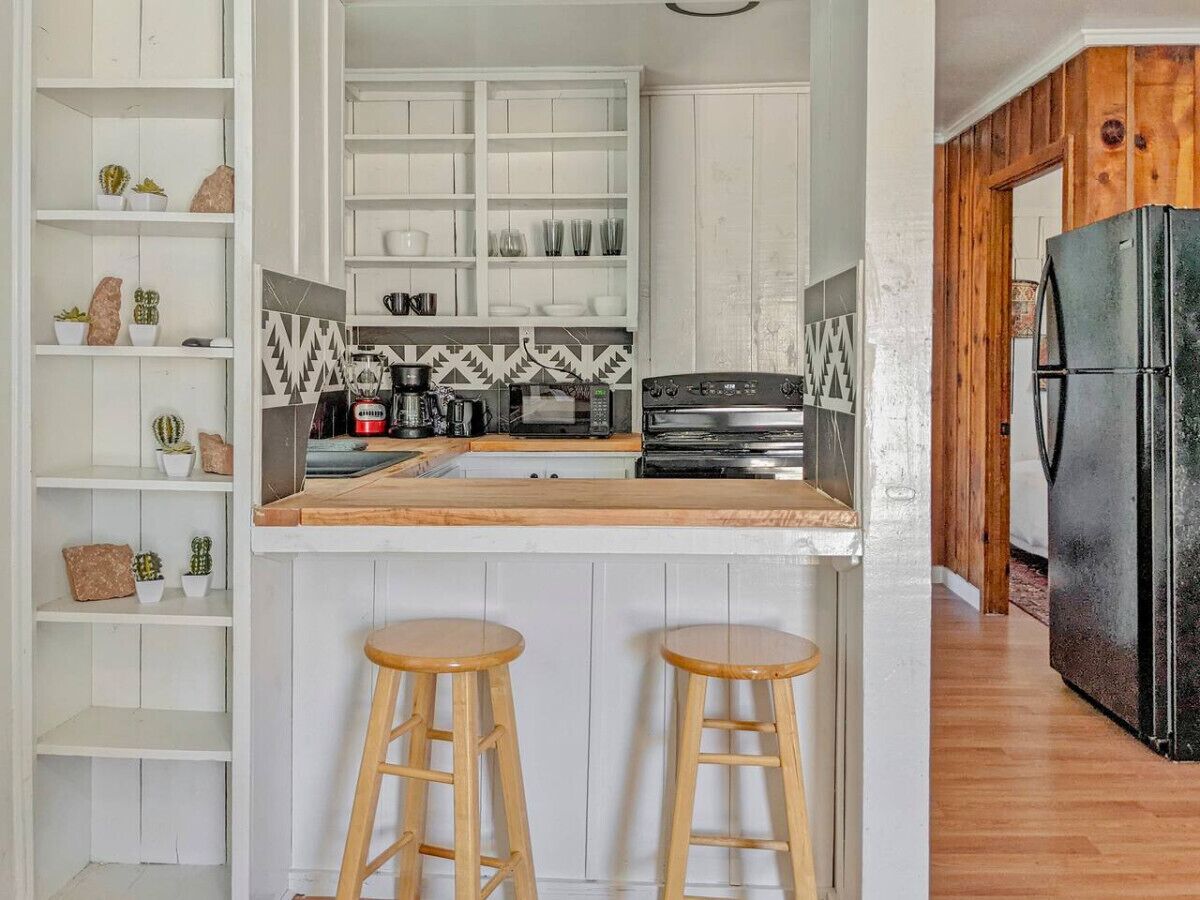 A kitchen with white cabinetry, a black refrigerator, and two wooden stools.