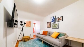 A living room with a grey sofa, colorful cushions, a blue rug, and framed artwork on the wall. - Downtown Kanab • Family & Pet Friendly • Hot Tub (Kanab)