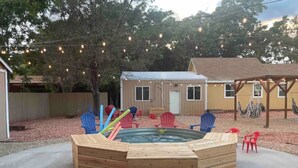 A wooden hot tub with a wooden deck, surrounded by outdoor chairs and string lights. - Downtown Kanab • Family & Pet Friendly • Hot Tub (Kanab)