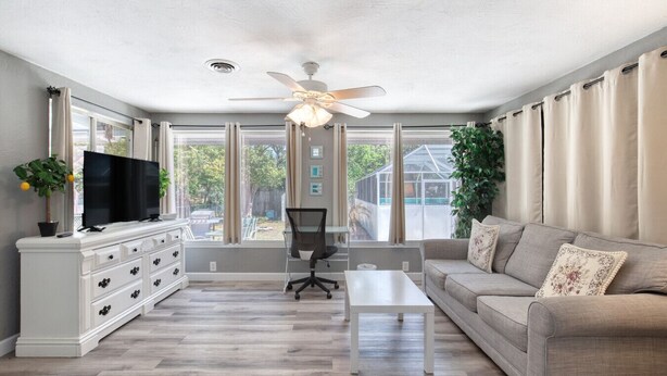 A spacious living room with a flat-screen TV, a ceiling fan, a sofa, and a coffee table. - Endless Summer Oasis with a Pool (Daytona Beach)