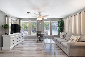 A spacious living room with a flat-screen TV, a ceiling fan, a sofa, and a coffee table. - Endless Summer Oasis with a Pool (Daytona Beach)