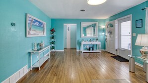 A room with teal walls, a wooden floor, a white console table with a mirror, a white door, and a ceiling fan. - Endless Summer Oasis with a Pool (Daytona Beach)