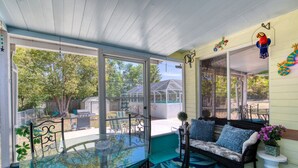 A covered patio with a glass table, a cushioned seating area, and a view of the backyard. - Endless Summer Oasis with a Pool (Daytona Beach)