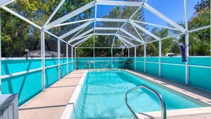 A covered swimming pool with a clear blue water, surrounded by a turquoise fence and white structural supports. - Endless Summer Oasis with a Pool (Daytona Beach)