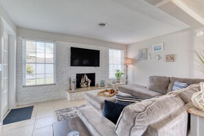 A living room with a fireplace, a flat-screen TV, a sofa, and a coffee table. - Cresting Wave Cottage by the Sea (Ormond Beach)