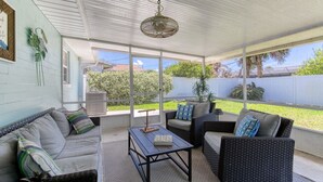 A covered patio with a sofa, chairs, and a table. - Cresting Wave Cottage by the Sea (Ormond Beach)