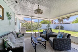 A covered patio with a sofa, chairs, and a table. - Cresting Wave Cottage by the Sea (Ormond Beach)