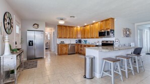A modern kitchen with wooden cabinets, stainless steel appliances, and a central island with stools. - Cresting Wave Cottage by the Sea (Ormond Beach)