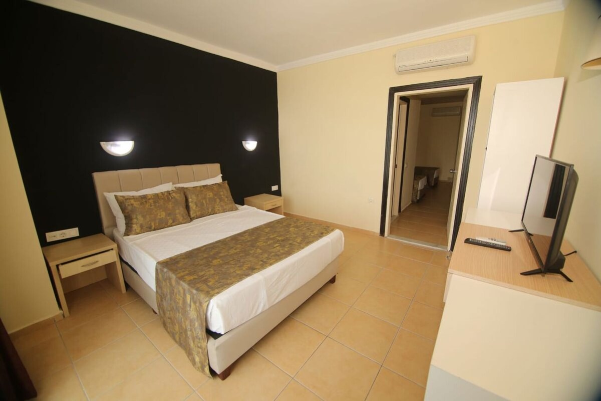 A hotel room with a bed, bedside tables, a TV, and a mirror.