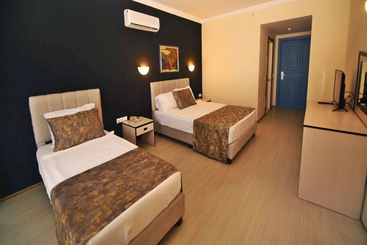 Quarto de hotel com duas camas, uma escrivaninha, uma cadeira, uma televisão e uma porta.
