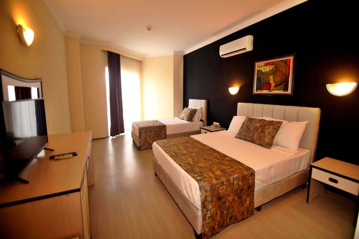 Quarto de hotel com duas camas, uma escrivaninha, televisão e um quadro na parede.