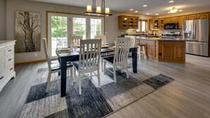 Une cuisine moderne avec des meubles en bois, des appareils en acier inoxydable et un coin repas comprenant des chaises blanches et une table foncée.