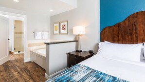 Ein Hotelzimmer mit einem Bett, einem Nachttisch, einer Lampe, einem Badezimmer mit Badewanne und zwei gerahmten Bildern an der Wand.