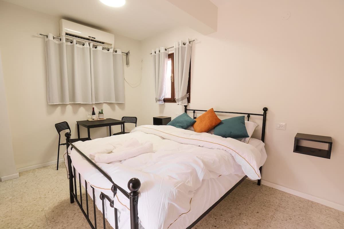 A bedroom with a bed, a desk, a chair, and a window with curtains.