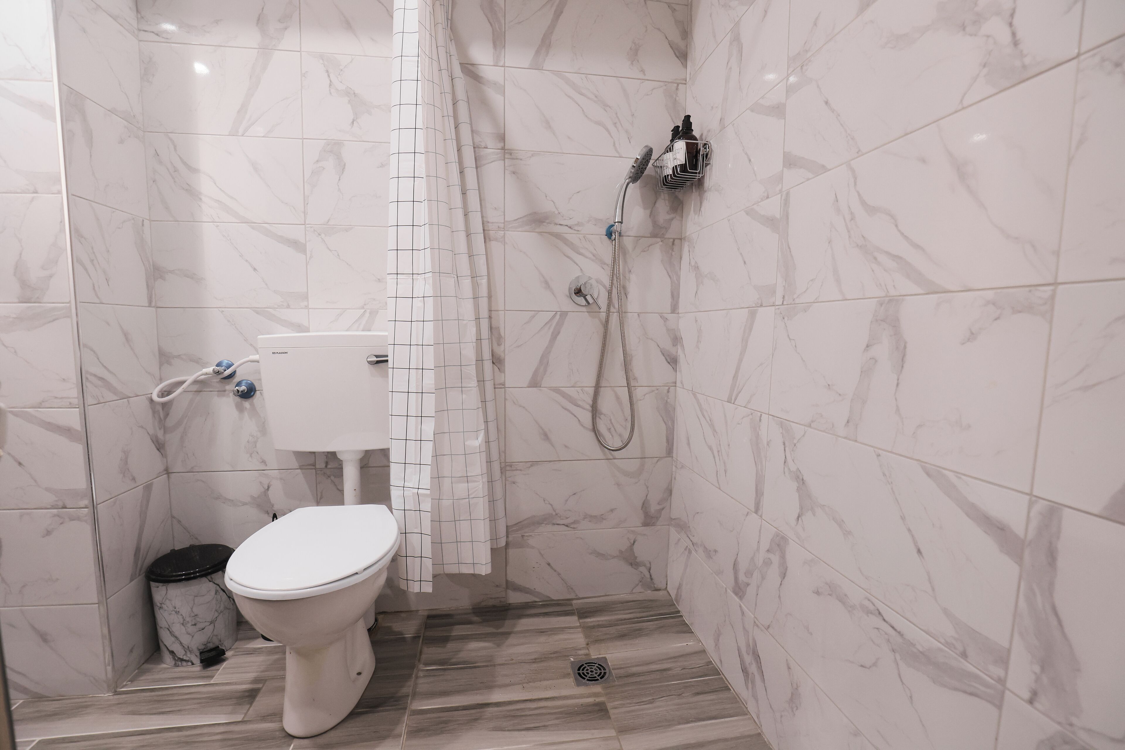 A bathroom with a toilet, a shower, and a marble-tiled wall.