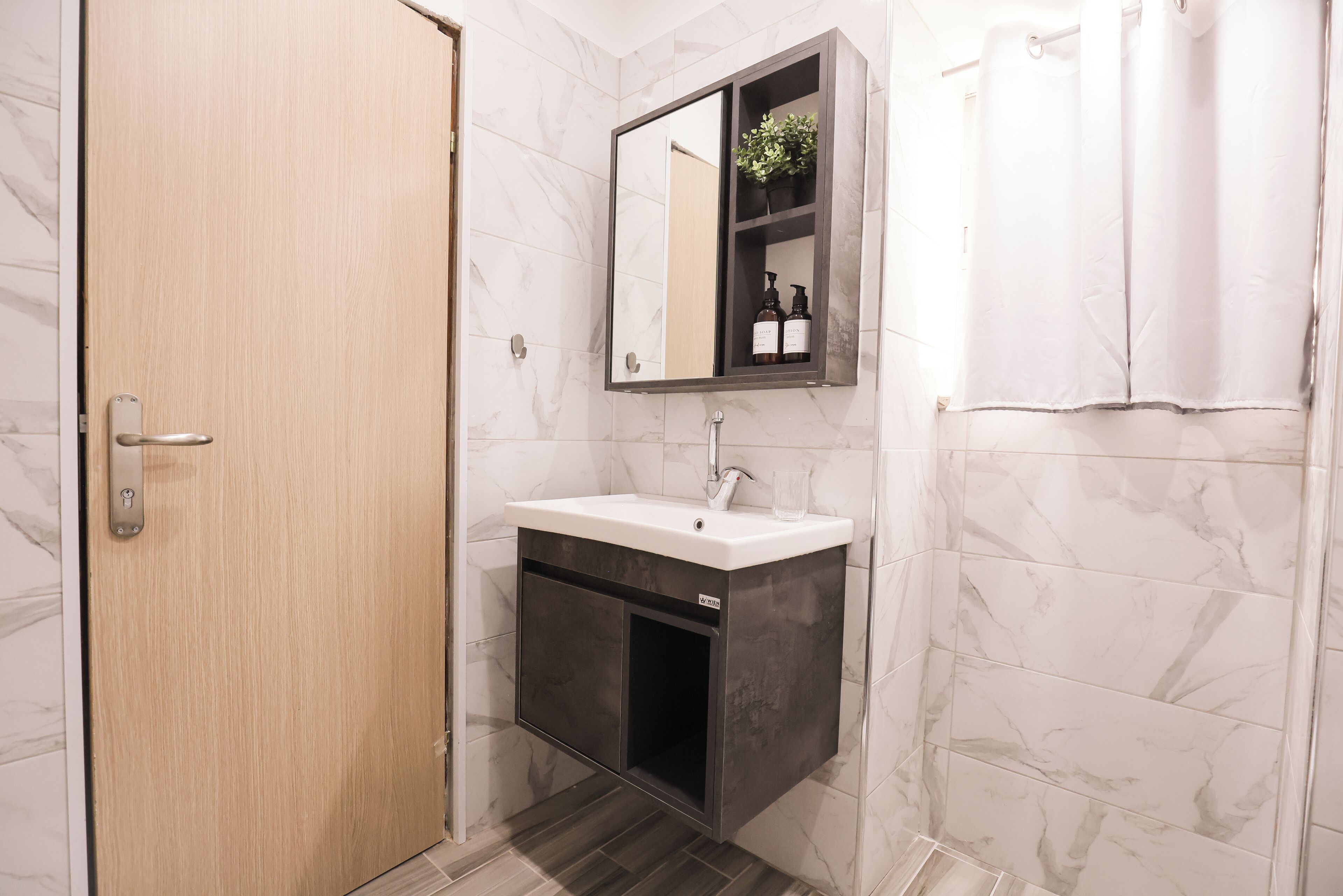 A bathroom with a wooden door, a white sink with a mirror above it, and a shower curtain.