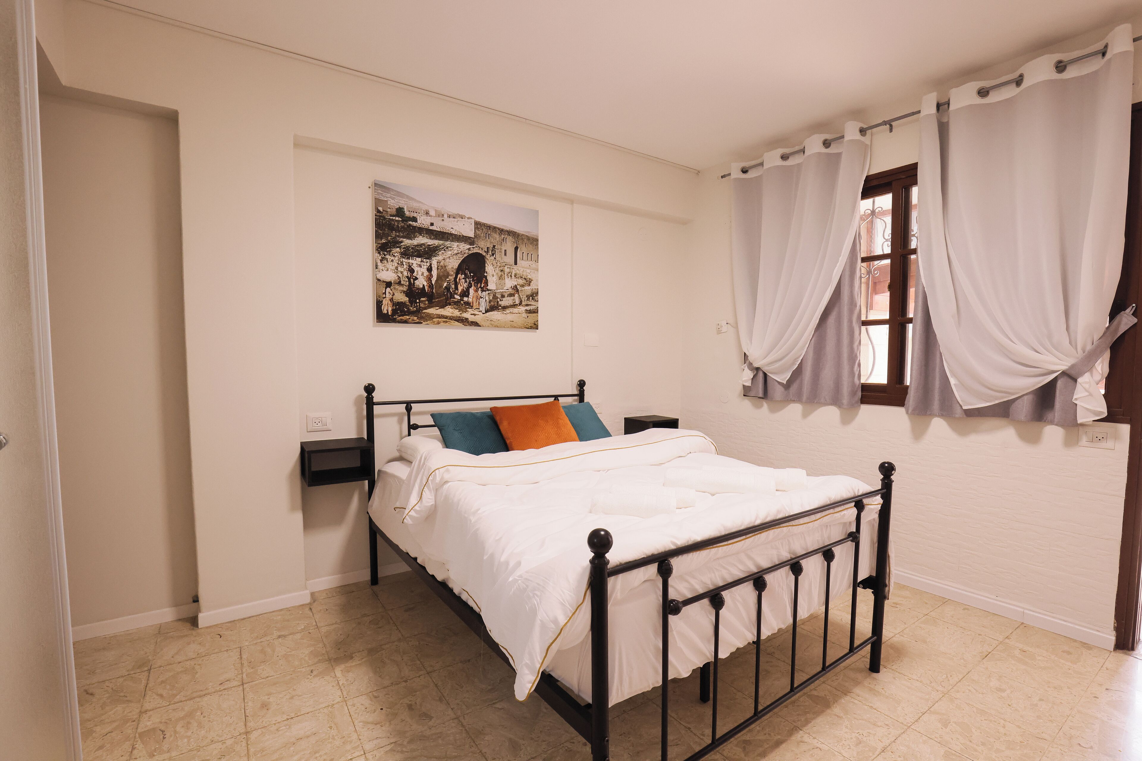 A bedroom with a bed, a nightstand, a wall-mounted picture, and a window with curtains.