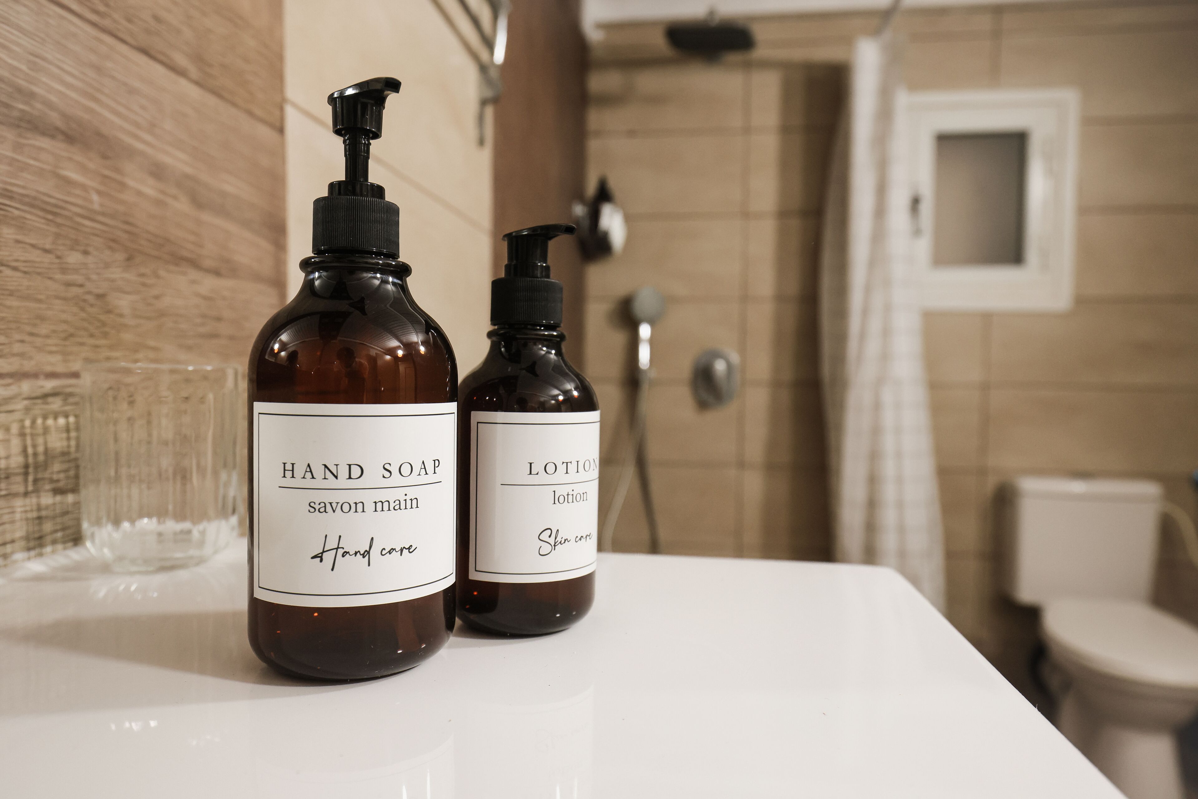 Two bottles of hand soap and lotion on a white countertop in a bathroom.