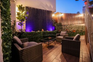 Un patio al aire libre con mobiliario de mimbre, una mesa con fruta y una pared decorativa con una fuente de agua.