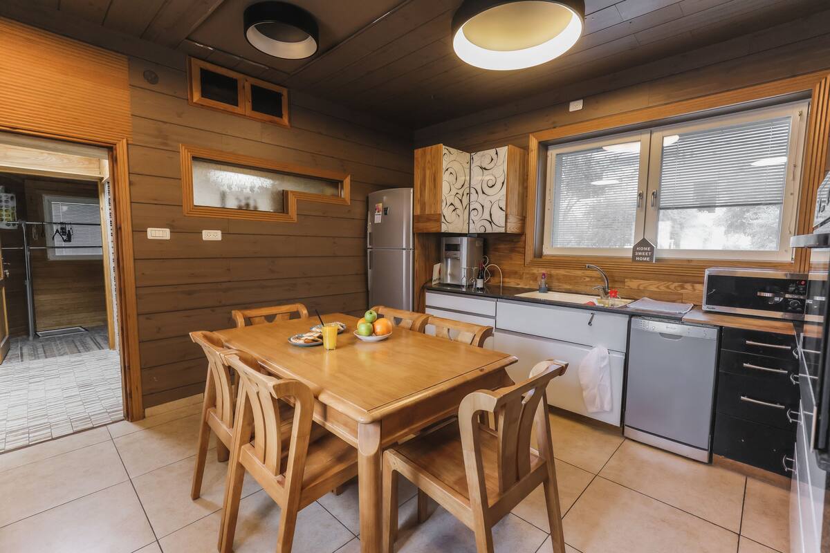 A modern kitchen with wooden cabinetry, a dining table with chairs, a refrigerator, a microwave, and a dishwasher.