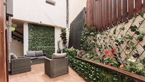 Een terras met rieten meubilair en een groene wand.