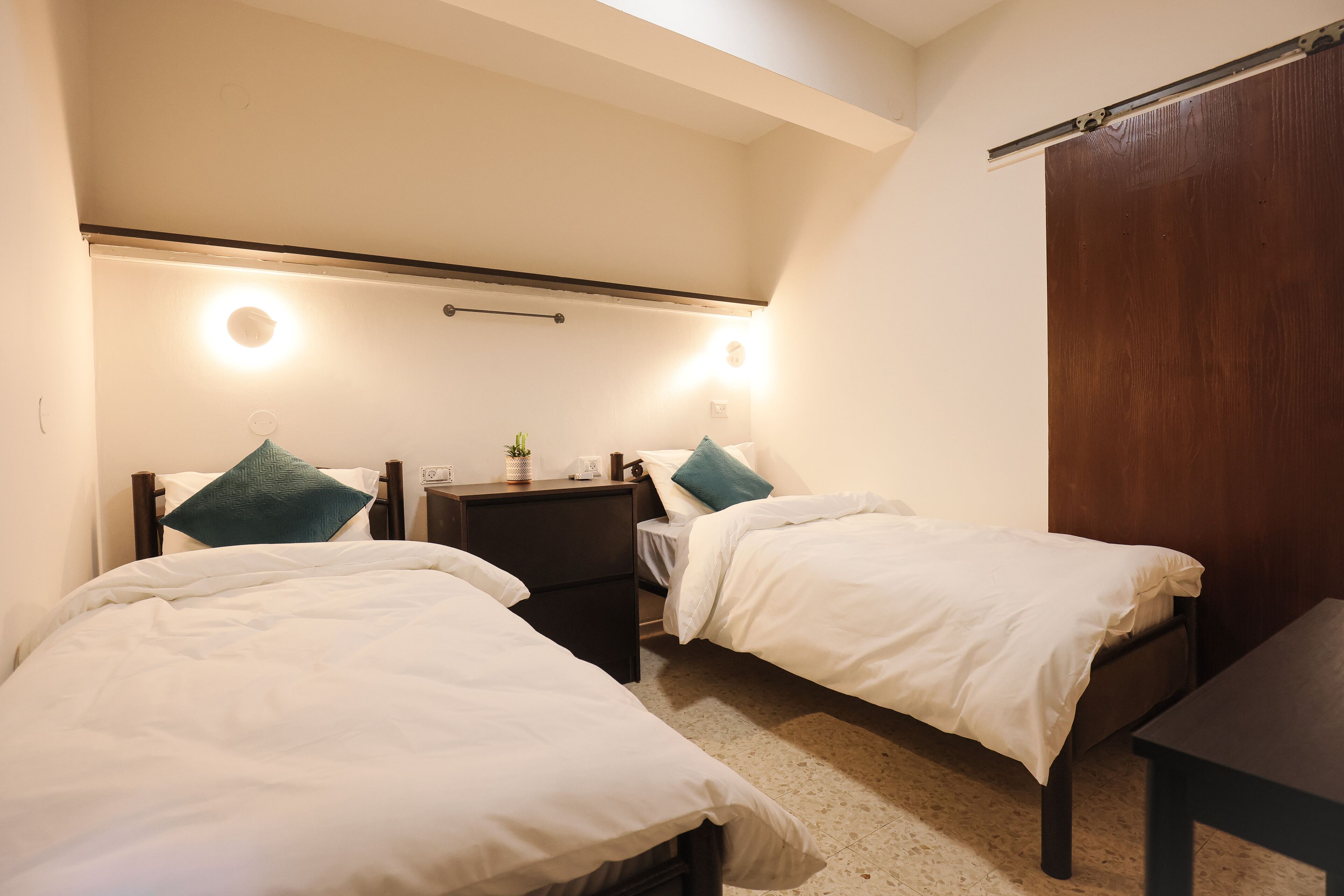 A bedroom with two single beds, a nightstand with a lamp, and a wooden wardrobe.