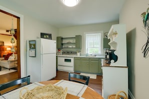 A compact kitchen with a refrigerator, stove, and cabinets. There is a dining table with chairs and a woven placemat. - Historic Home on Farm, 15 Mi to Williamsport! (Jersey Shore)