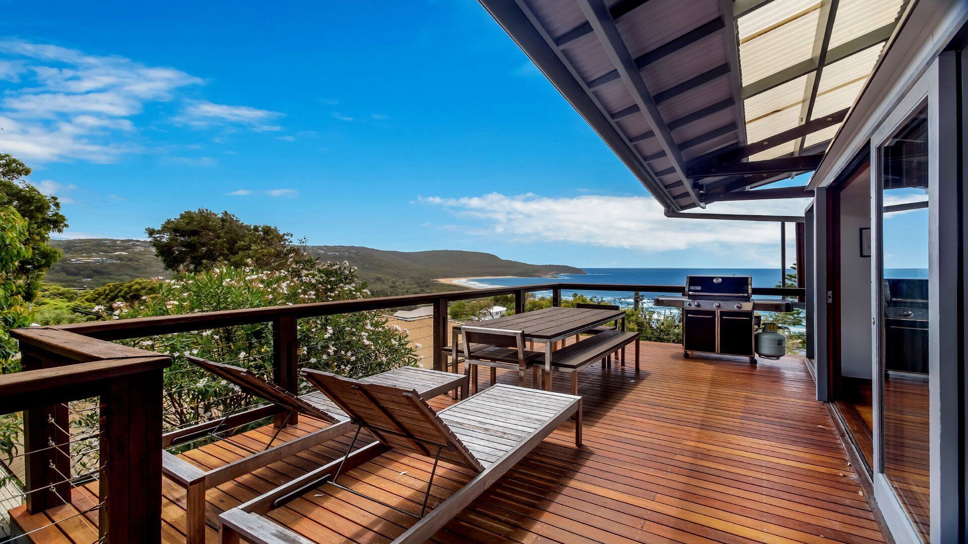 Una terraza de madera con una mesa y sillas, con vista a una playa y al océano.