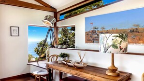 A dining area with a wooden table, chairs, a tripod-mounted light, and artwork on the walls. - Atlas - House for all seasons, spa with ocean views and cozy fireplace (KILLCARE)