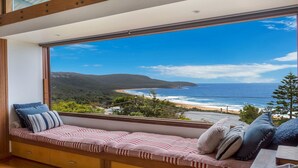 A room with a large window offering a view of a beach and ocean. - Atlas - House for all seasons, spa with ocean views and cozy fireplace (KILLCARE)