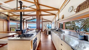 A modern kitchen with wooden beams, a large window overlooking a scenic view, and a dining area with a view. - Atlas - House for all seasons, spa with ocean views and cozy fireplace (KILLCARE)