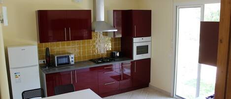 A compact kitchen with red cabinets, a microwave, stove, and a dishwasher.