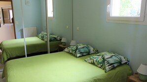 Huoneessa on kaksi sänkyä, joissa on vihreät vuodevaatteet ja samanväriset tyynyt. Huoneessa on myös ikkuna, josta tulee luonnonvaloa, ja seinällä on peili.